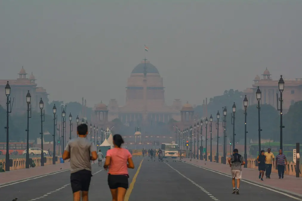 Two joggers on a hazy Delhi avenue with Rashtrapati Bhavan faint in the smog behind them