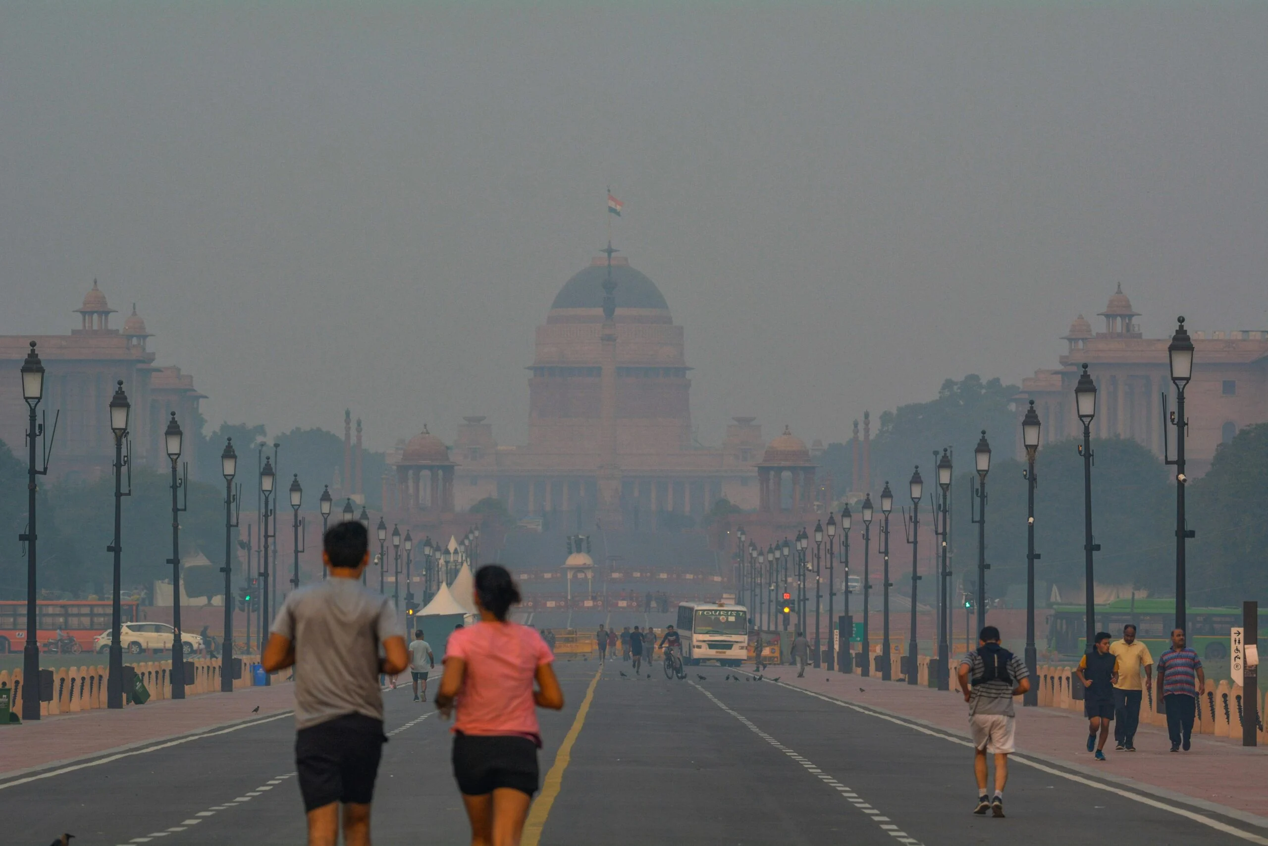 Two joggers on a hazy Delhi avenue with Rashtrapati Bhavan faint in the smog behind them