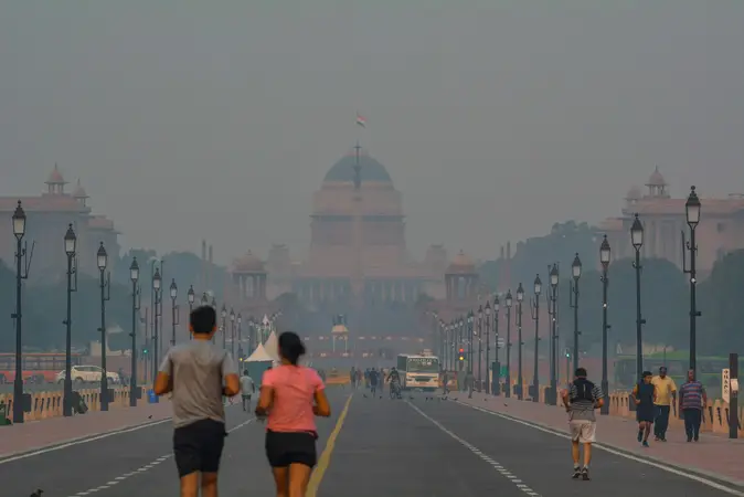 Two joggers on a hazy Delhi avenue with Rashtrapati Bhavan faint in the smog behind them