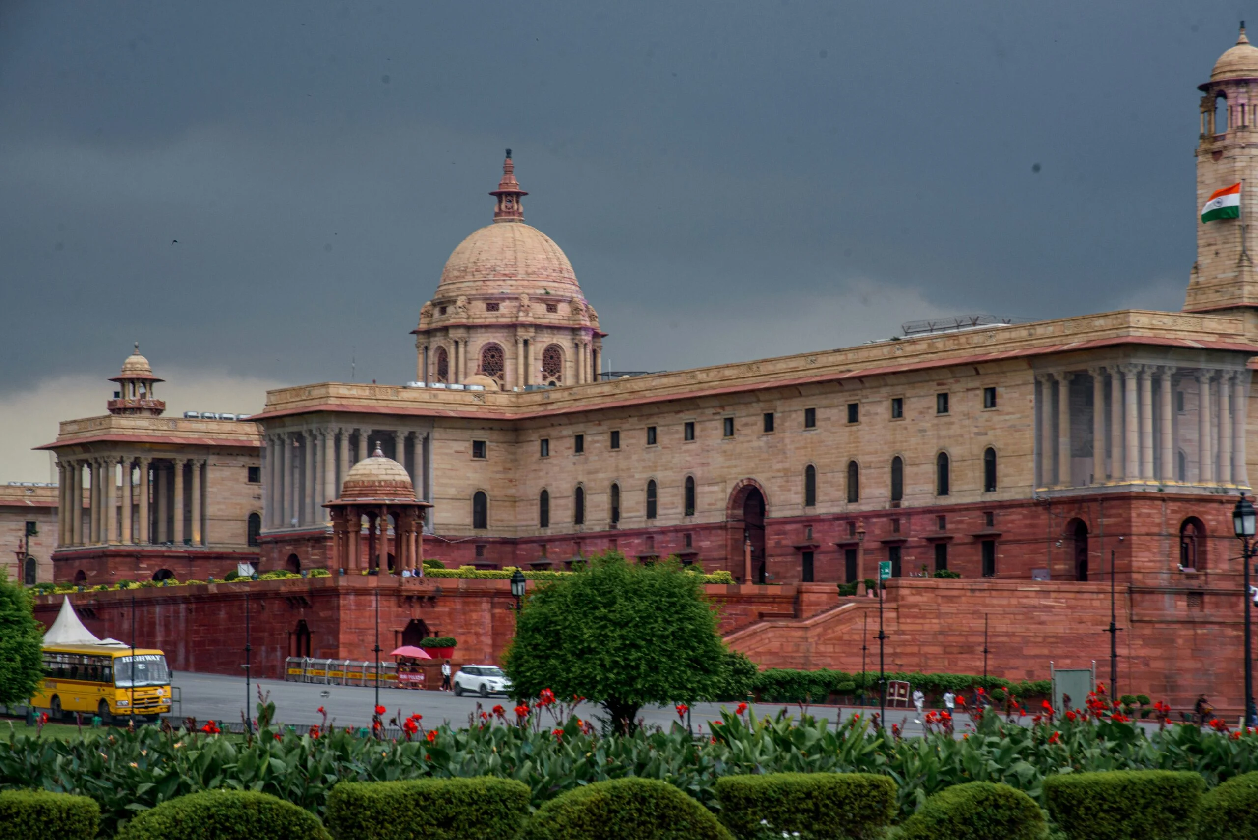 Rashtrapati Bhavan sandstone building in New Delhi under a dark cloudy sky with the Indian flag flying