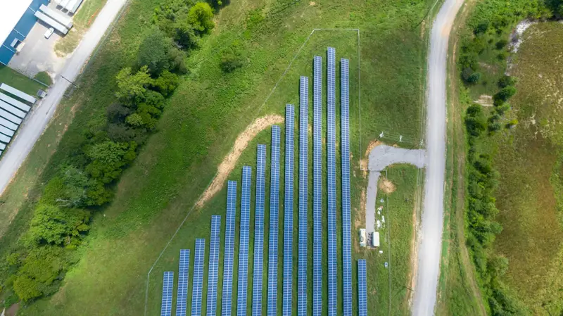 Aerial view of rows of solar panels on a grassy field beside a gravel road
