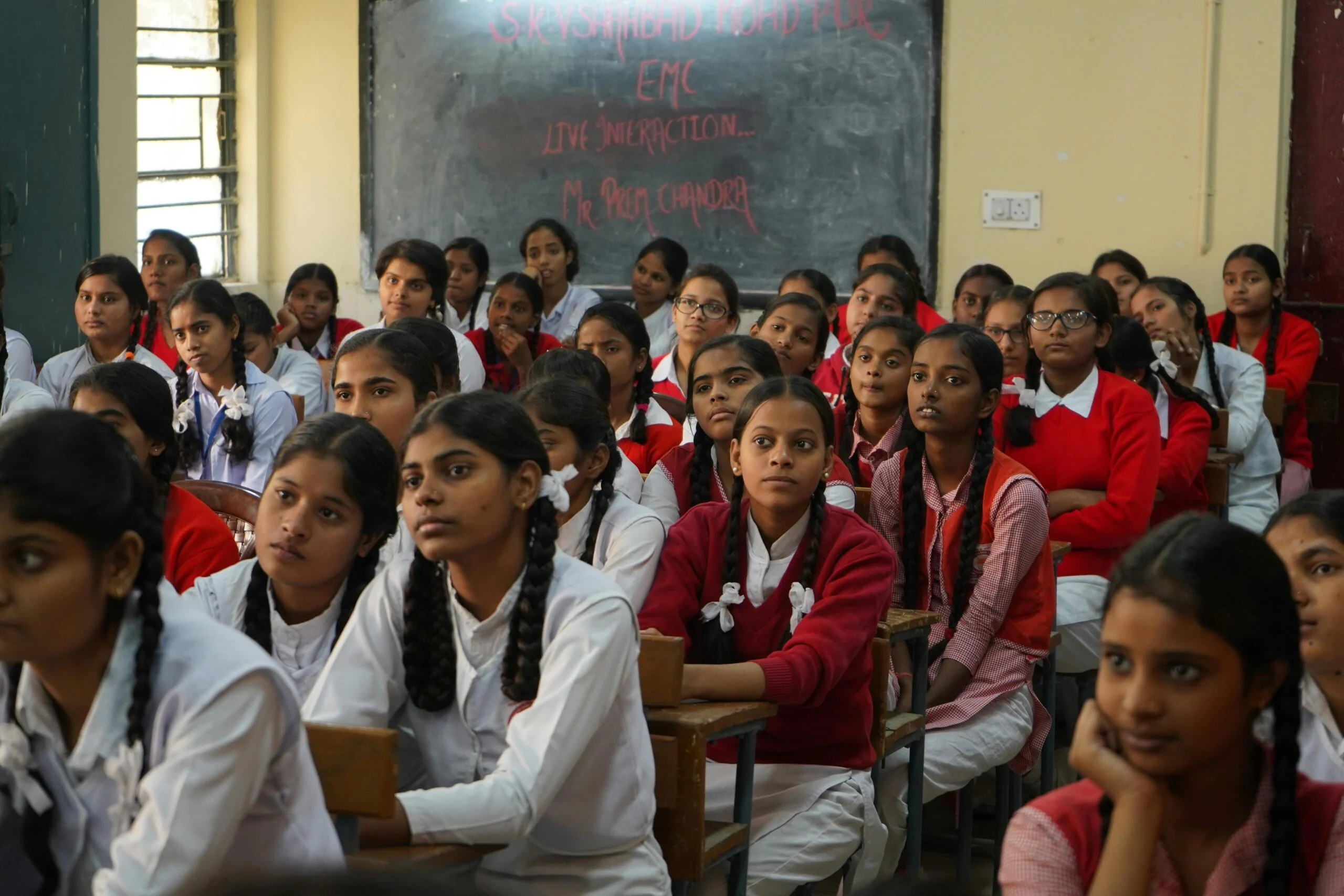 Schoolgirls in uniform sitting at desks in a classroom, looking toward the front