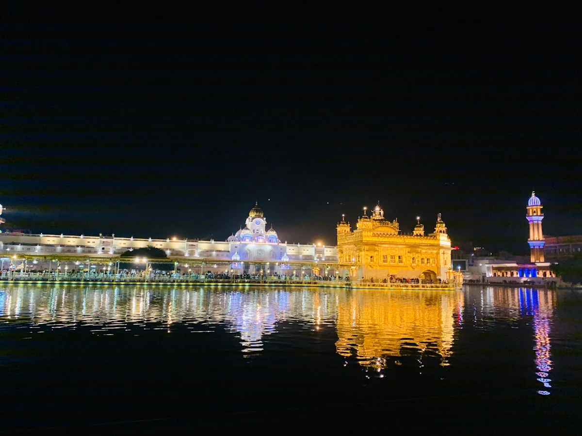 Golden Temple in Amritsar lit up at night, with its golden reflection on the dark water and a blue-lit minaret beside it