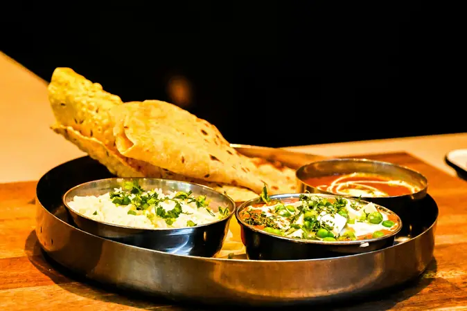 Steel thali with papad, rice and two bowls of vegetable curries garnished with herbs on a wooden table