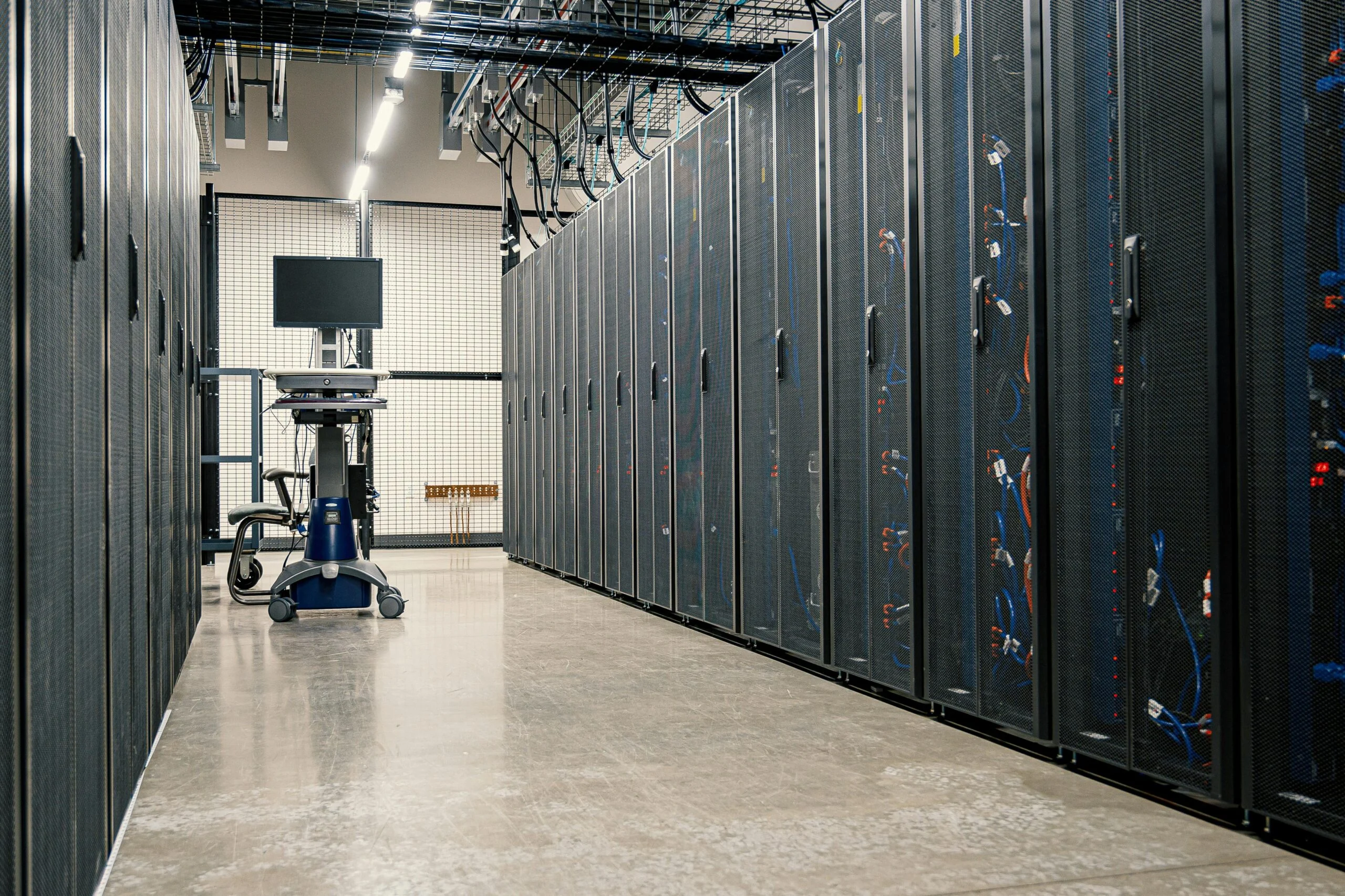 Long aisle of server racks in a data centre with a monitor on a wheeled stand at the end