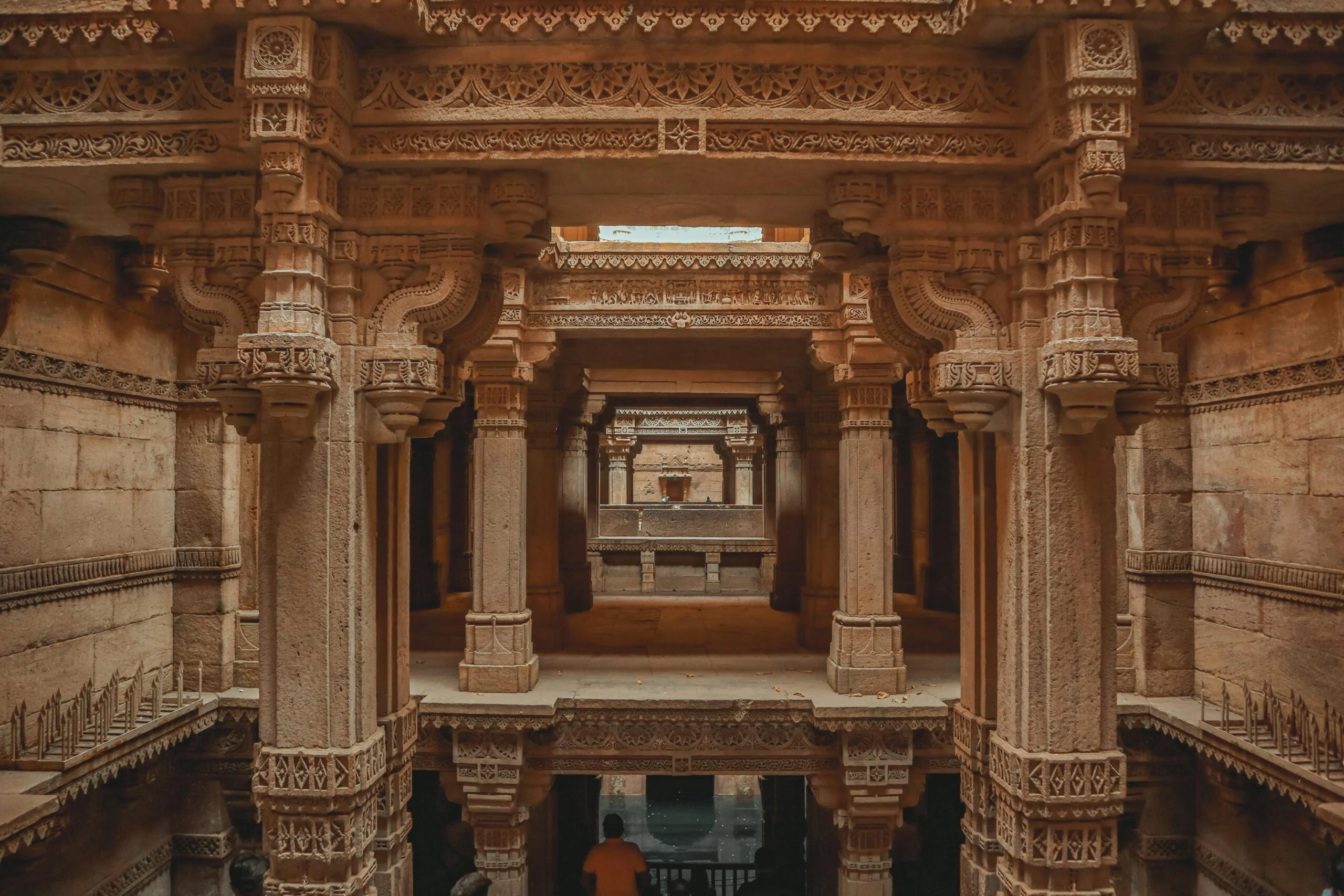 Carved sandstone pillars and tiered galleries of a historic stepwell with a person standing below