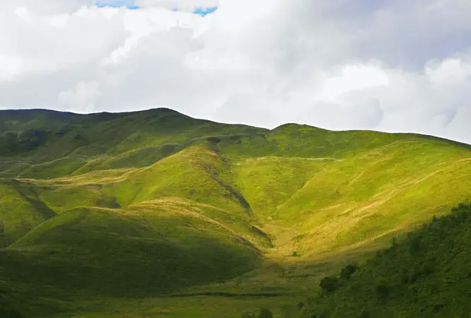 Green grassy hills lit by patches of sunlight under a cloudy sky