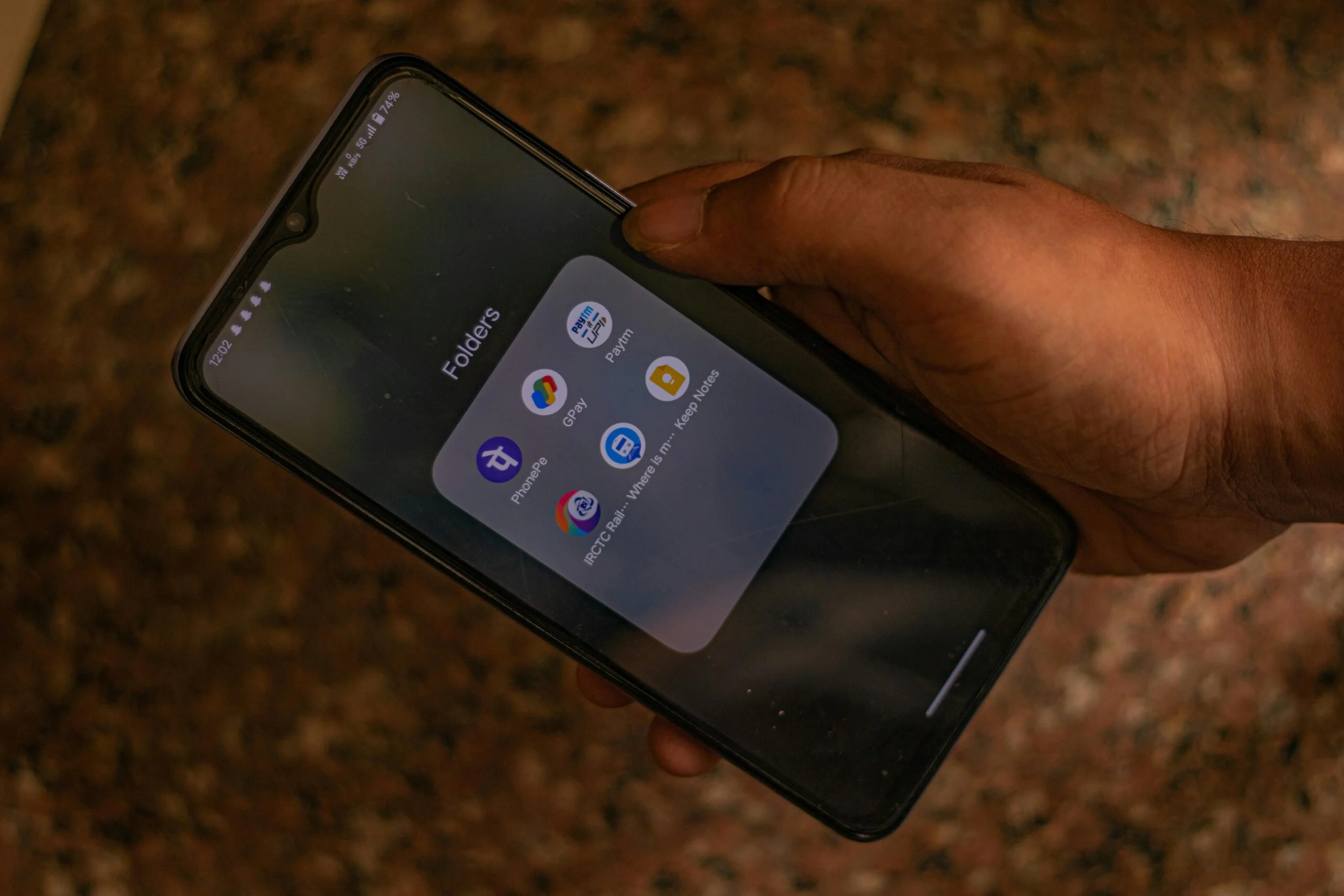 Hand holding a smartphone with a folder of payment apps including PhonePe, GPay and Paytm