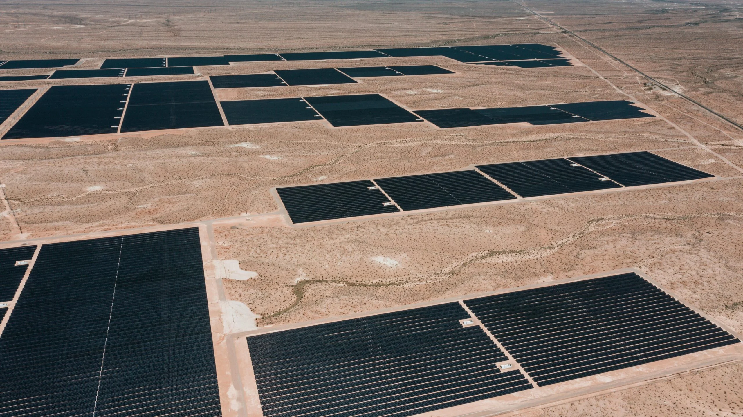 Aerial view of large dark solar panel arrays spread across dry desert land