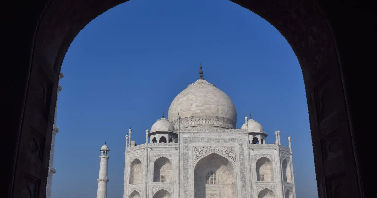 Taj Mahal framed by a dark arched doorway against a clear blue sky