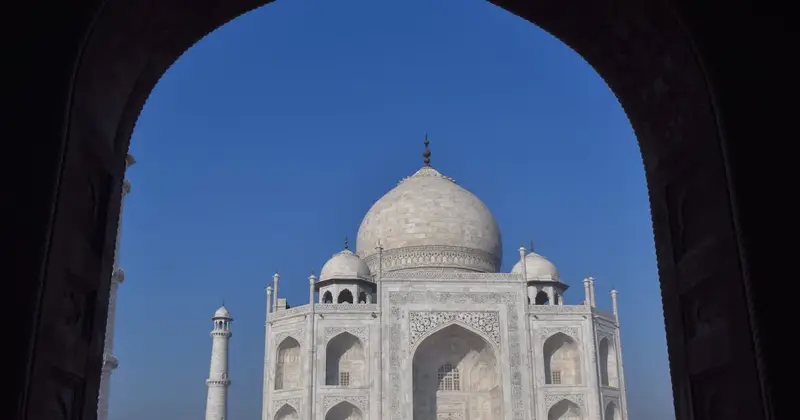 Taj Mahal framed by a dark arched doorway against a clear blue sky