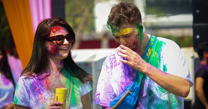 Two people laughing with faces and clothes covered in purple, green, yellow and red Holi powder