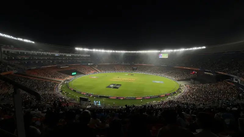 Floodlit cricket stadium at night with a packed crowd around a green field