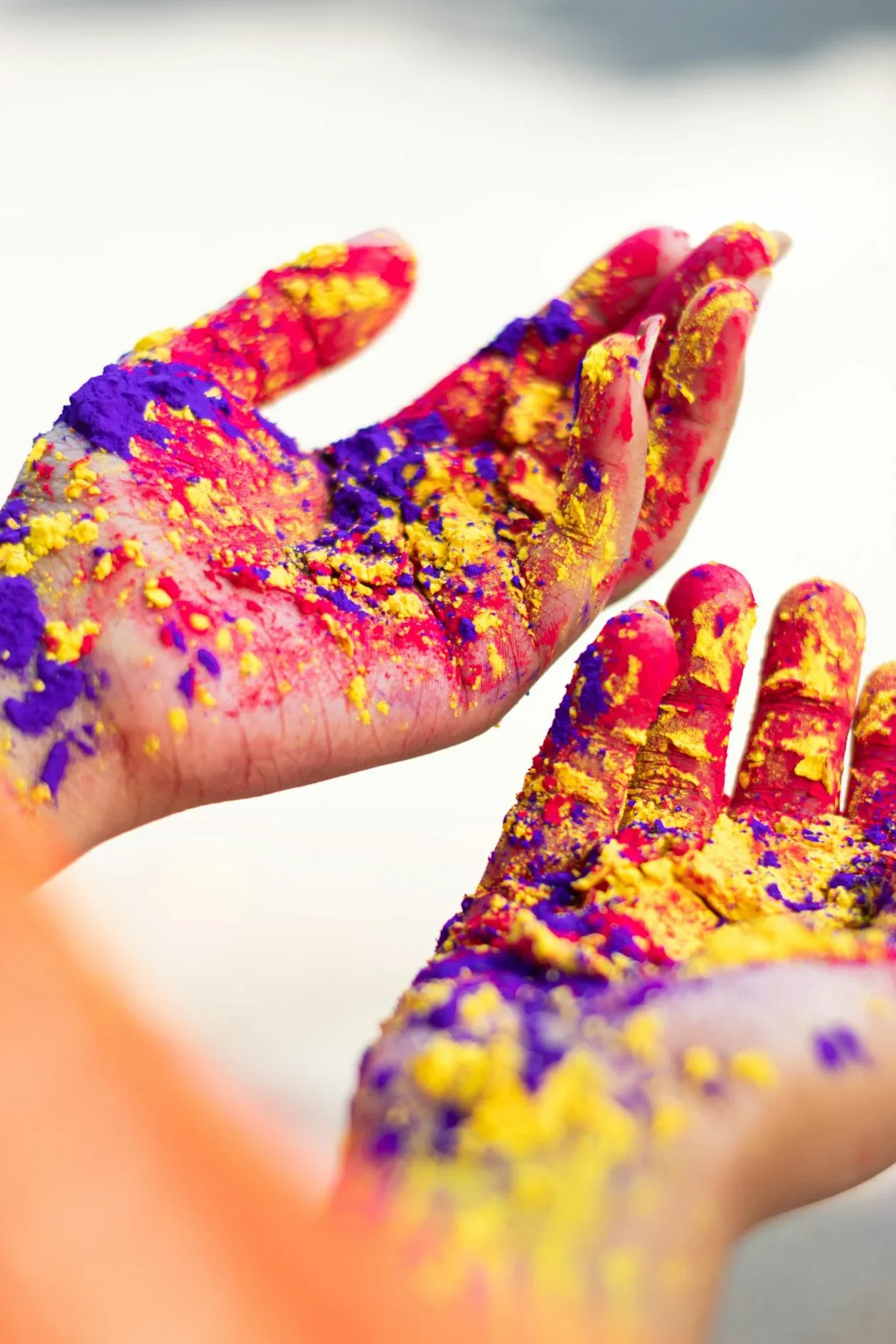 Two open hands covered in pink, yellow and purple Holi powder