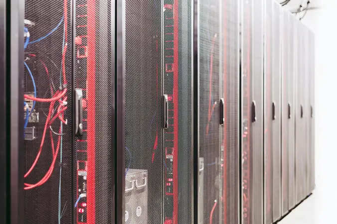 Rows of black server rack cabinets in a data centre with red and blue network cables visible through the mesh doors