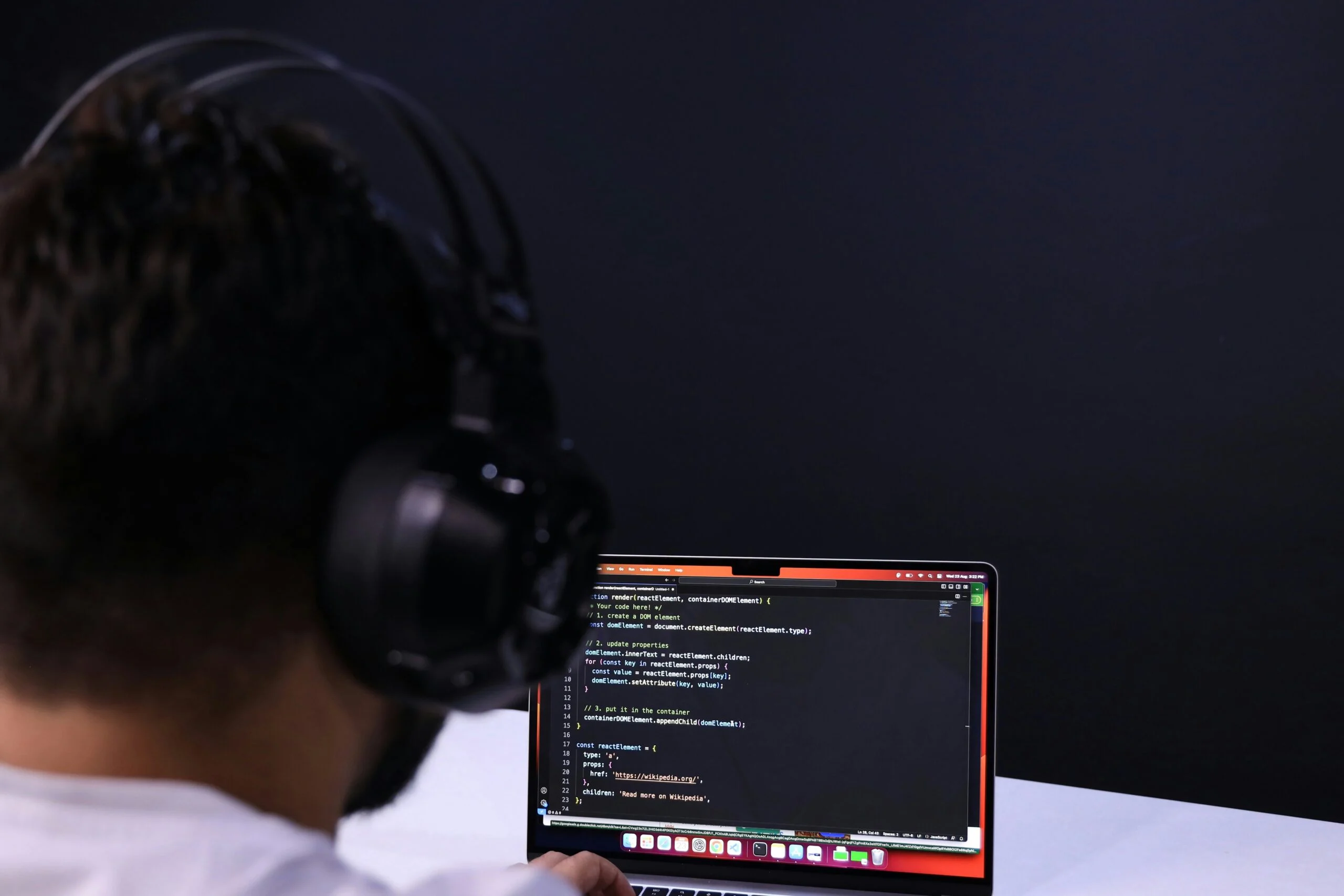 Person wearing large black headphones seen from behind looking at code on a laptop screen