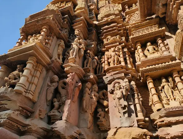 Close-up of a sandstone temple wall covered in carved figures, pillars and tiered mouldings under a blue sky