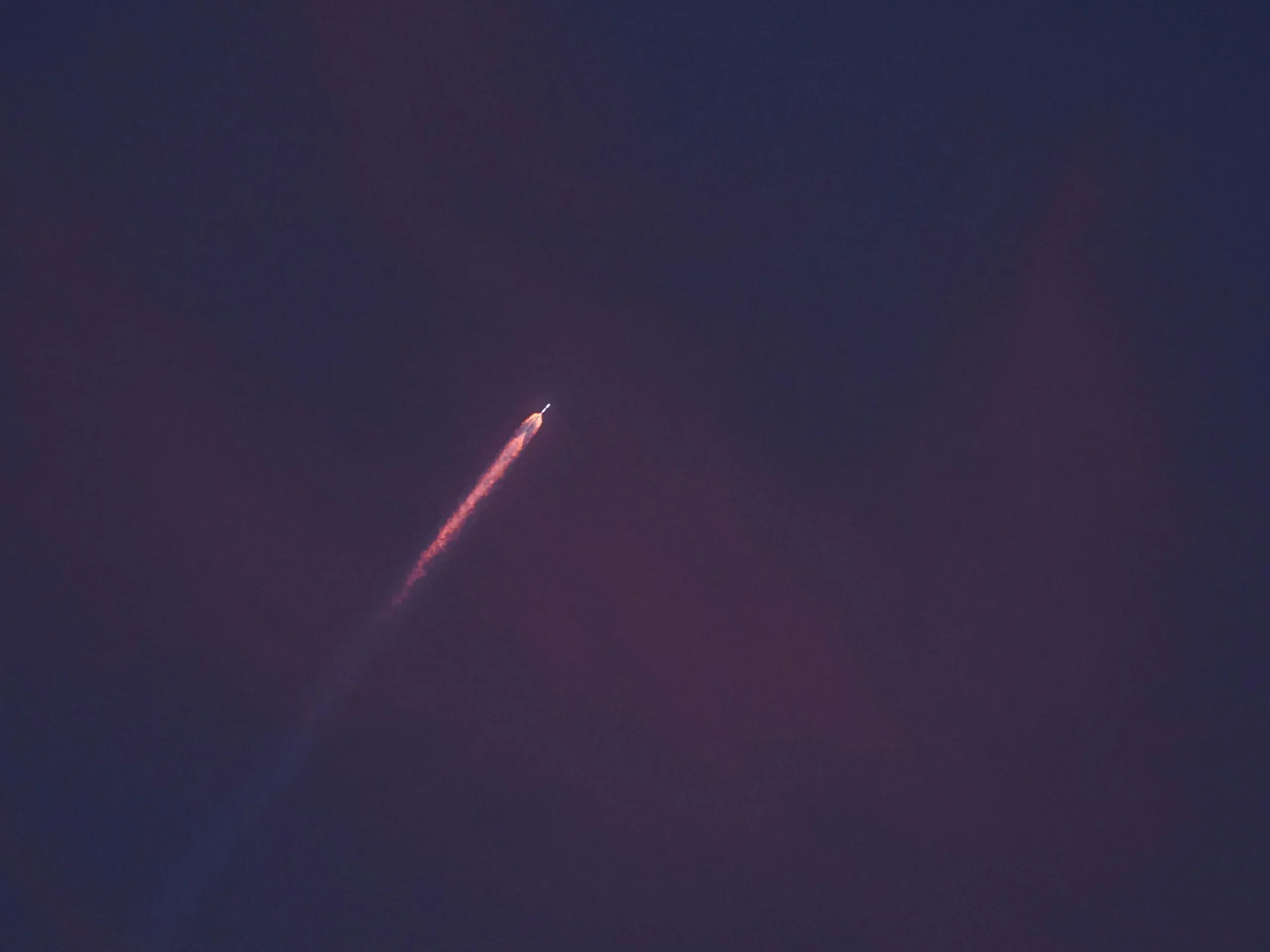 Small rocket with a glowing orange exhaust trail climbing through a dark purple twilight sky