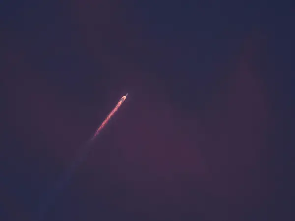Small rocket with a glowing orange exhaust trail climbing through a dark purple twilight sky