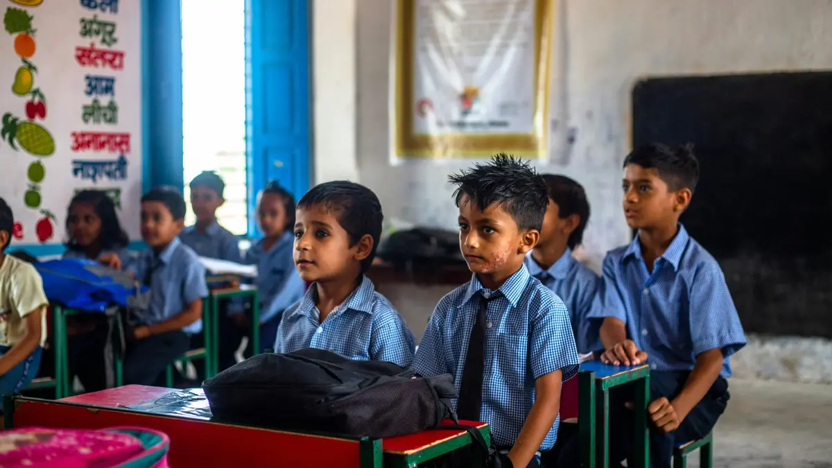 Schoolboys in blue uniforms sitting at red and green desks in a classroom