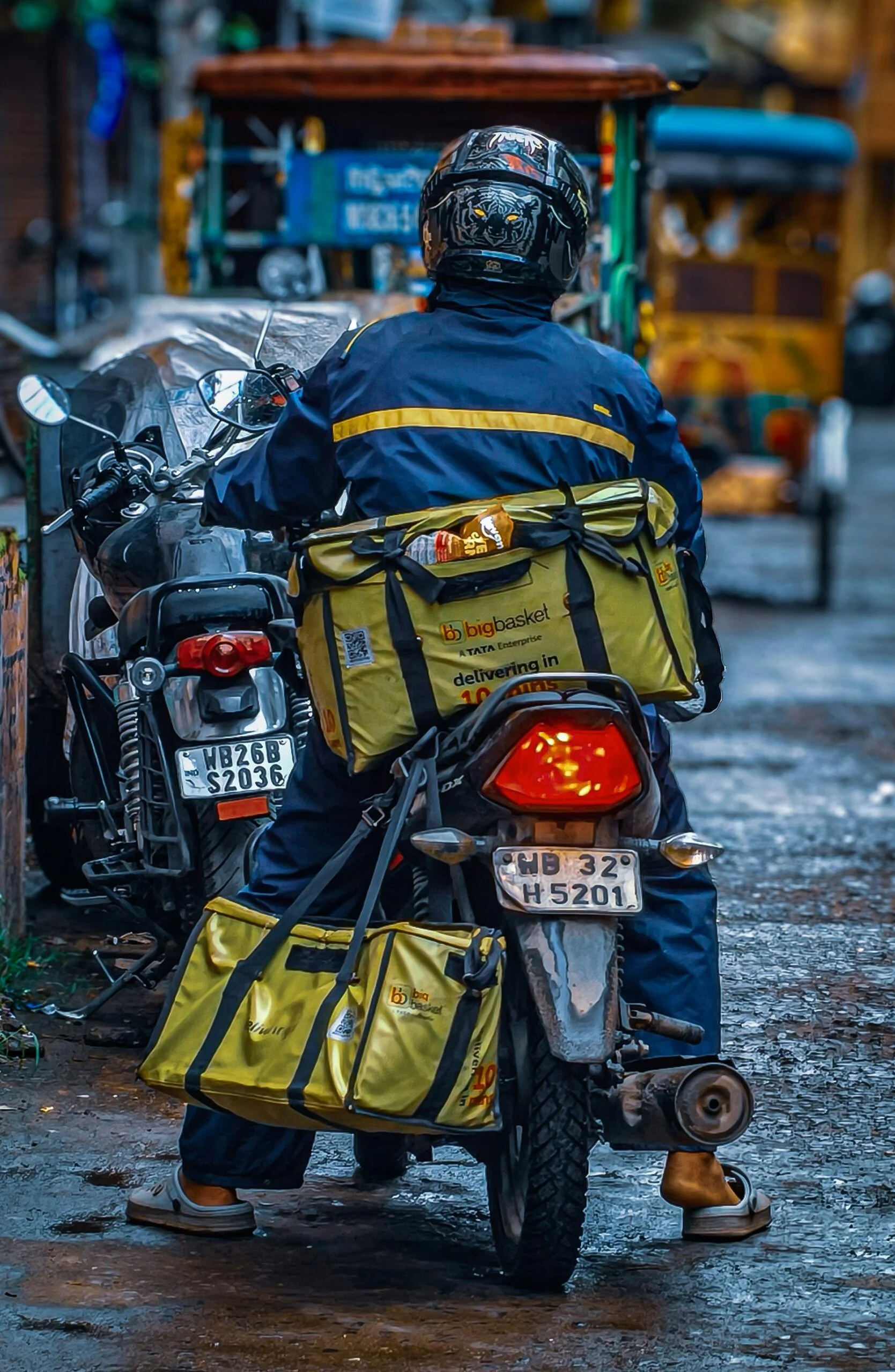 Delivery rider in a helmet and blue jacket on a motorbike with yellow delivery bags on a wet street