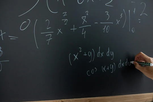 Hand writing integral and cosine equations in white chalk on a dark blackboard