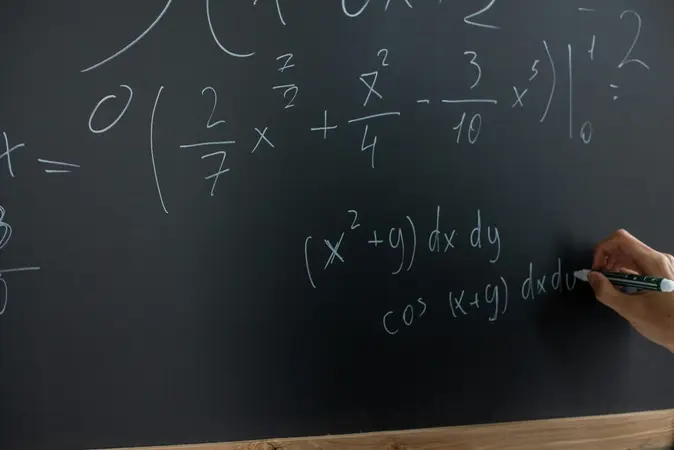 Hand writing integral and cosine equations in white chalk on a dark blackboard