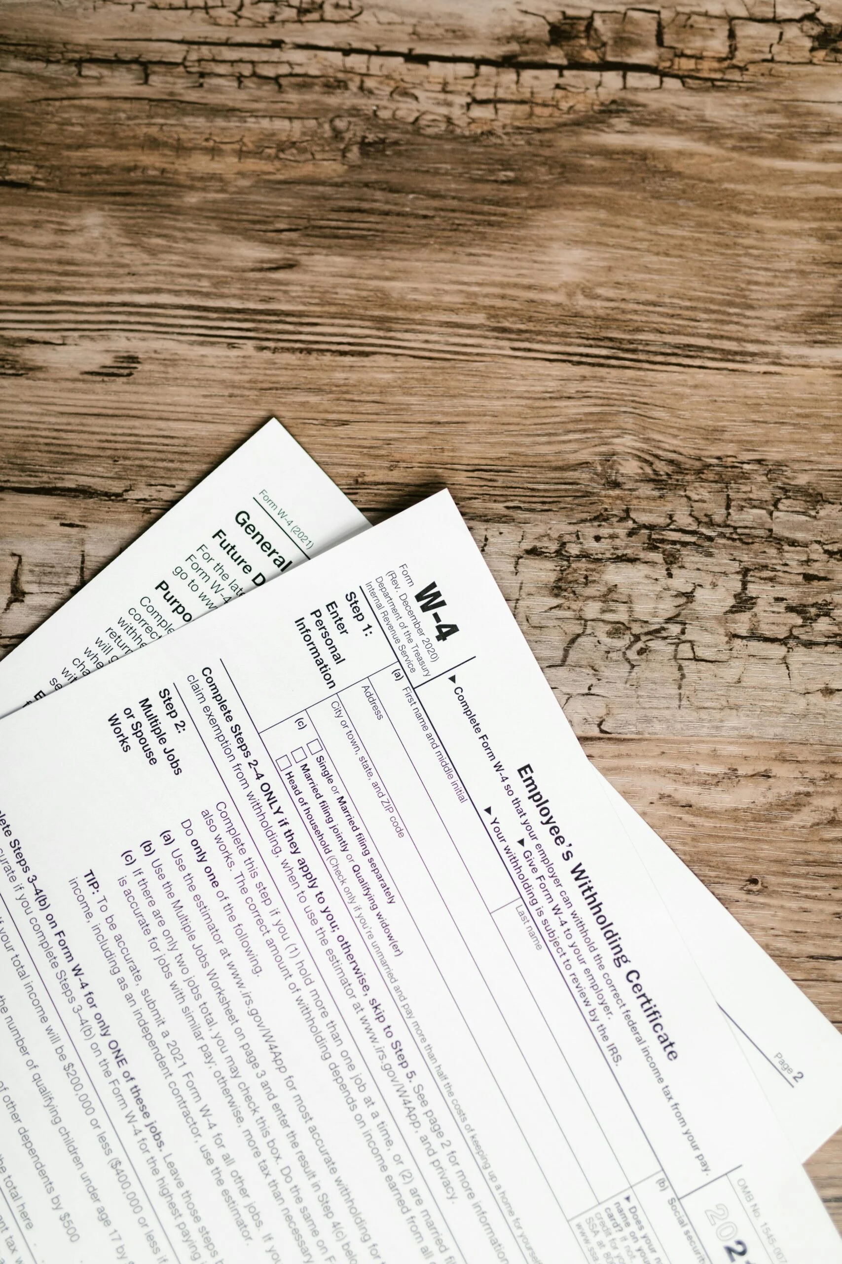 Paper forms labelled W-4 Employee's Withholding Certificate lying on a worn wooden table