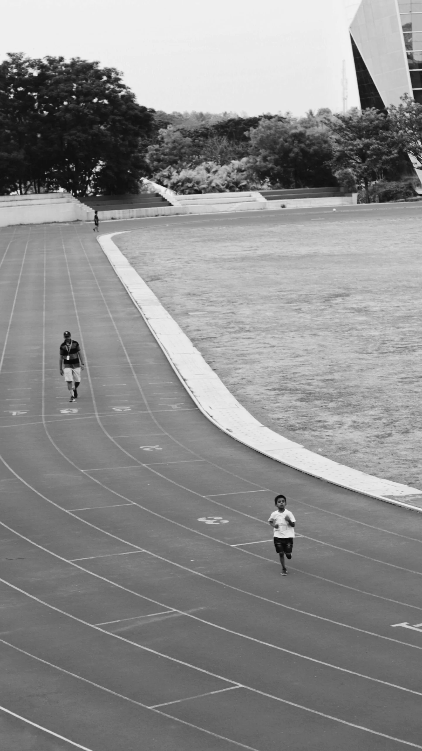 Black and white view of a running track with a child running and an adult walking in the distance