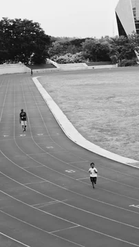 Black and white view of a running track with a child running and an adult walking in the distance