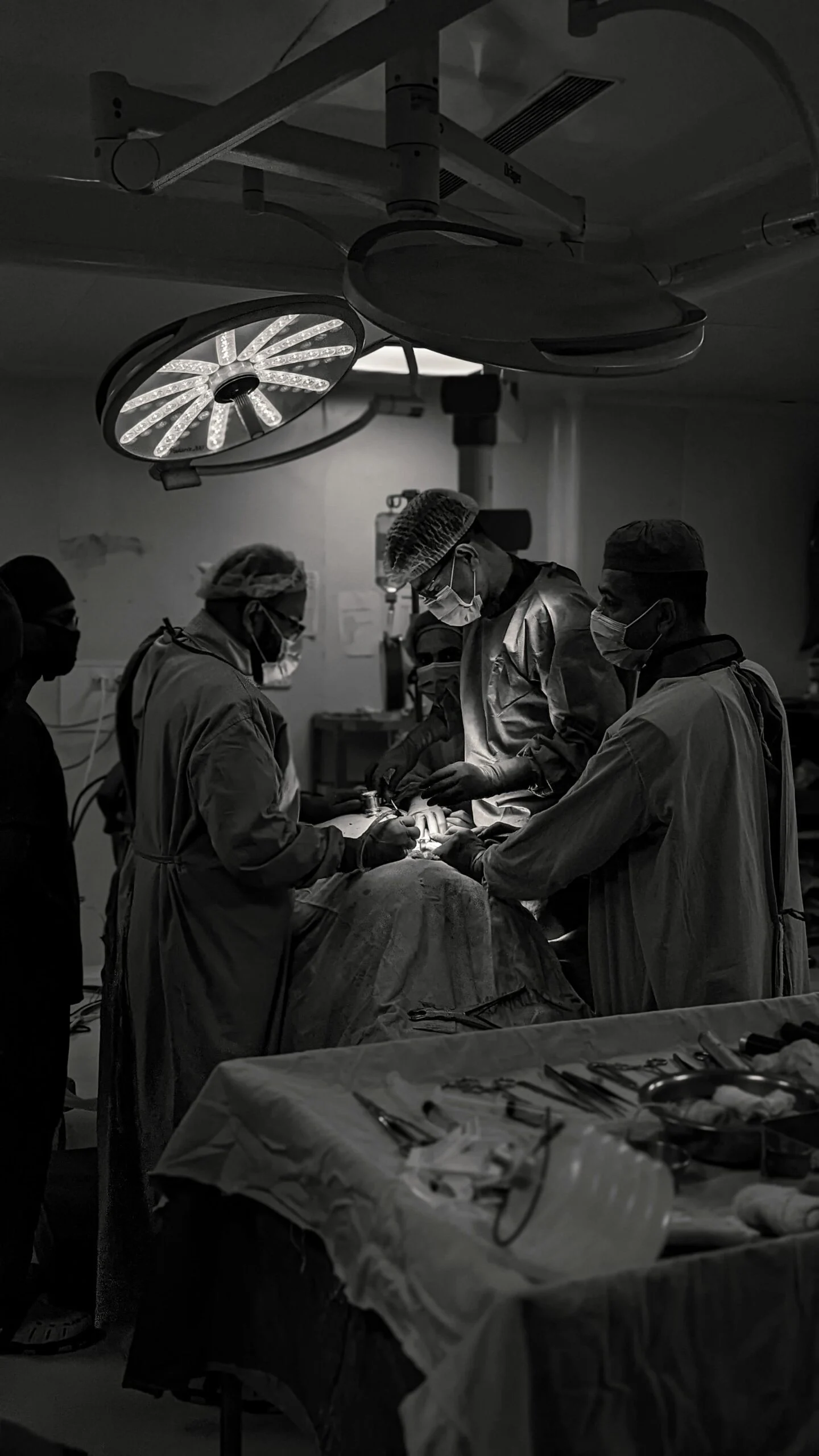 Black and white photo of surgeons operating under a bright surgical lamp in an operating theatre