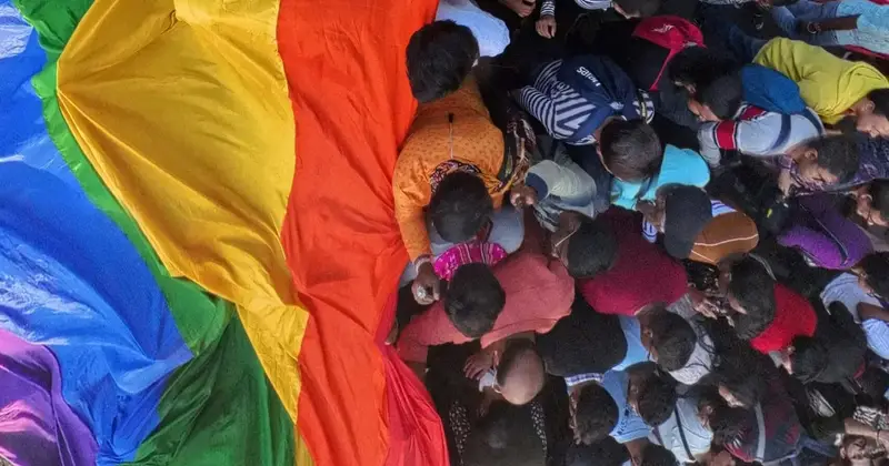 Crowd of people seen from above gathered around a large rainbow pride flag spread on the ground