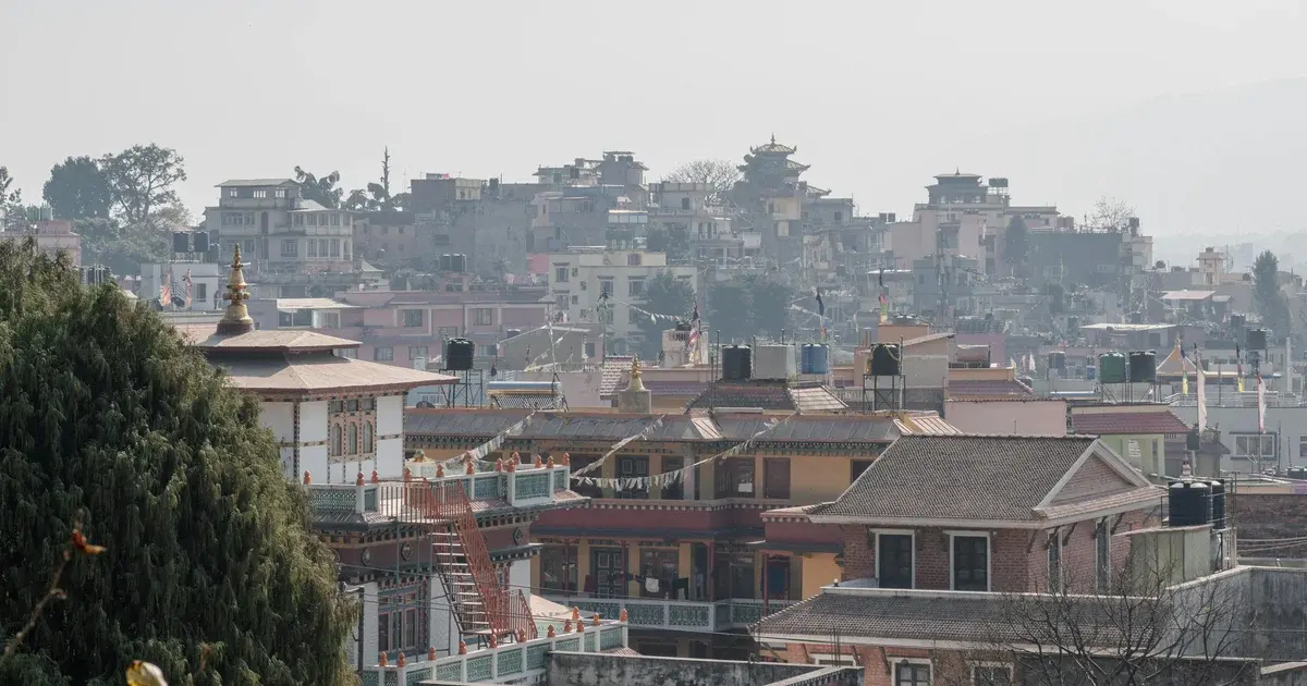 Hazy hillside view of Nepali rooftops, water tanks and a pagoda-style temple with prayer flags strung between buildings