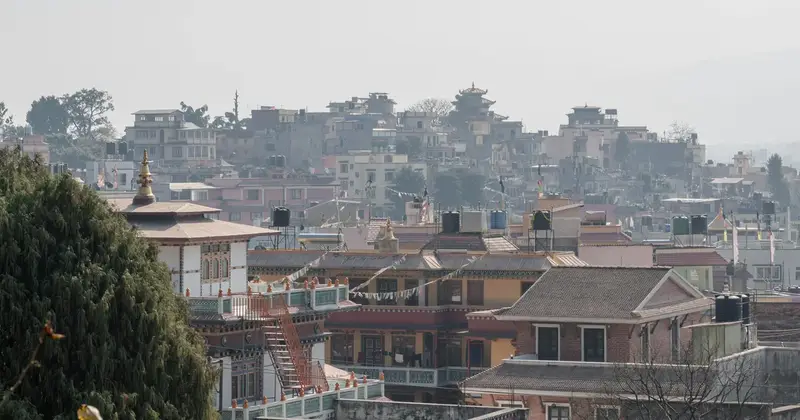 Hazy hillside view of Nepali rooftops, water tanks and a pagoda-style temple with prayer flags strung between buildings