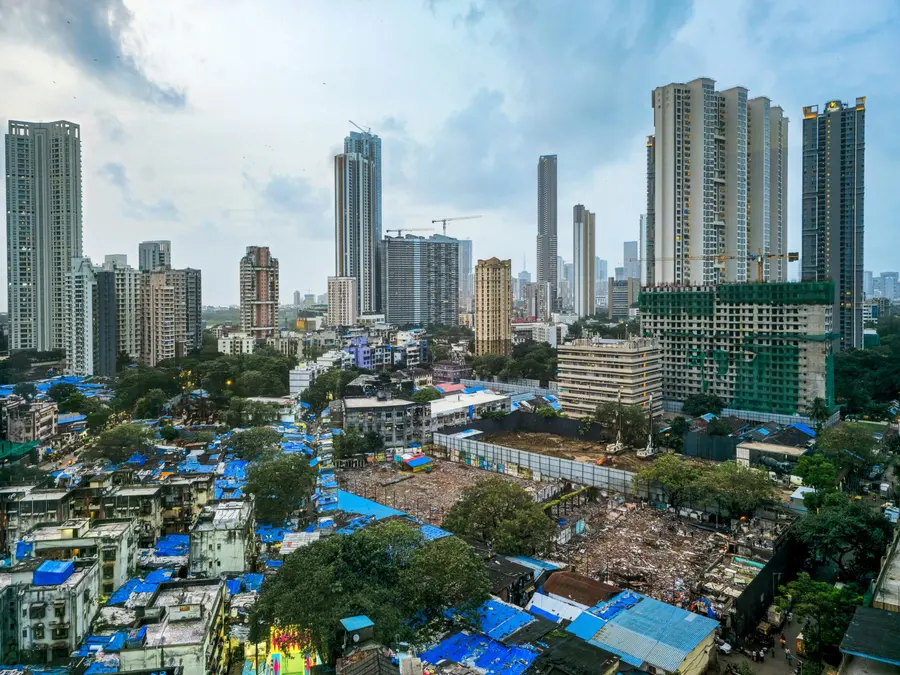 Mumbai skyline with tall residential towers and cranes rising above low buildings covered in blue tarpaulin roofs