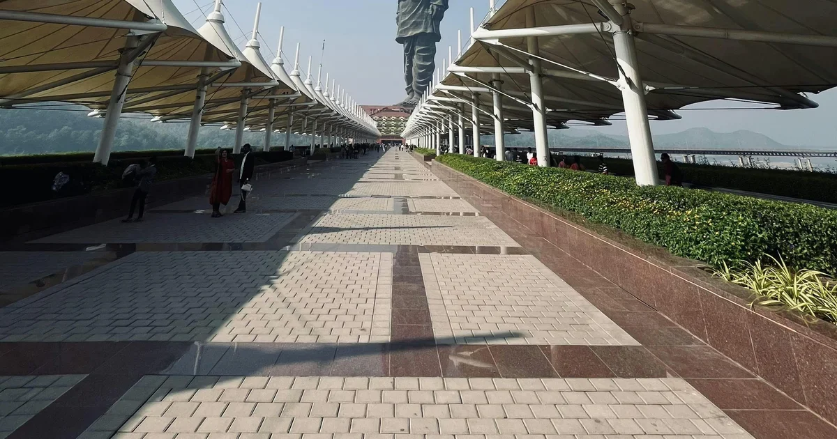 Paved walkway under white tensile canopies leading toward a tall statue in the distance