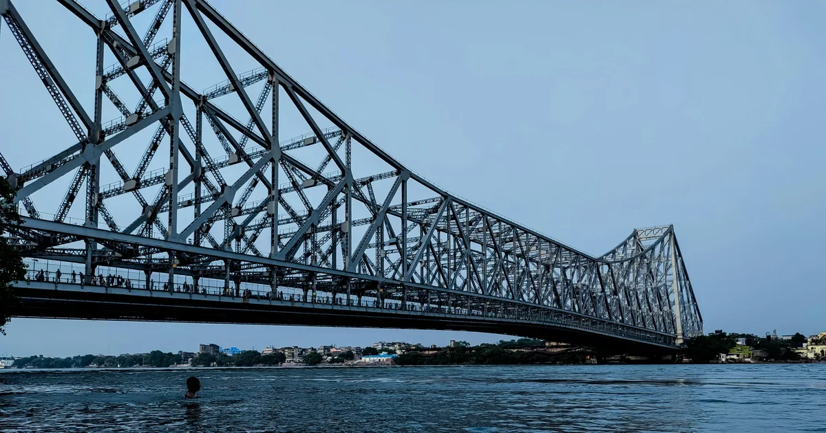 Steel cantilever bridge over a wide river, with a person swimming in the water below