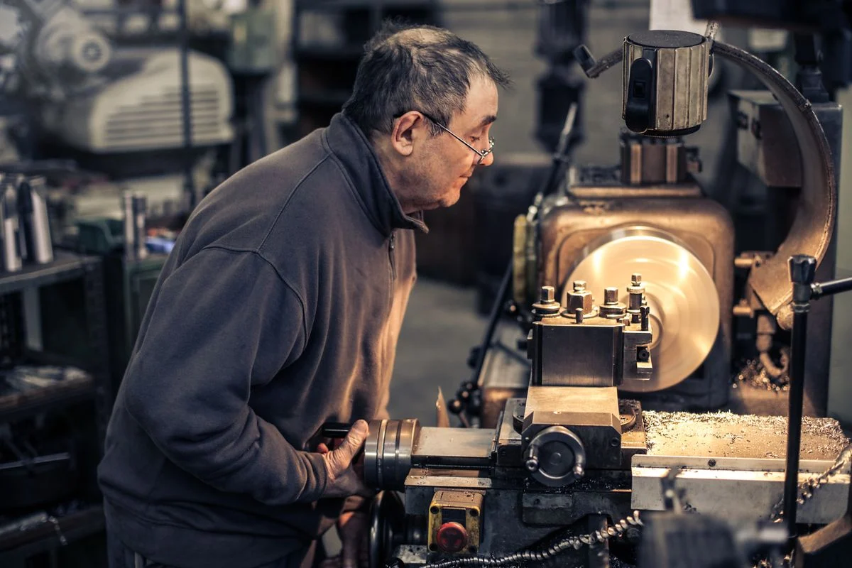 Man with glasses operating a metal lathe in a workshop