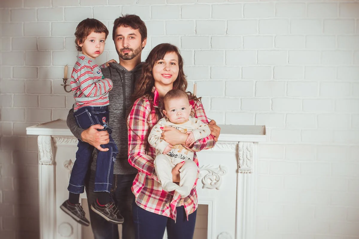 Family of four, a man, a woman and two small children, posing in front of a white brick wall