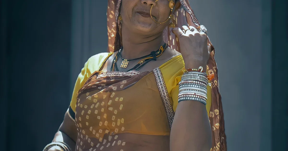 Woman in a yellow and brown sari with a nose ring and stacked bangles, face partly out of frame