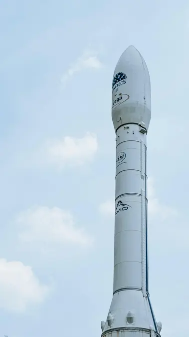 White Vega rocket standing upright against a pale blue sky with light clouds