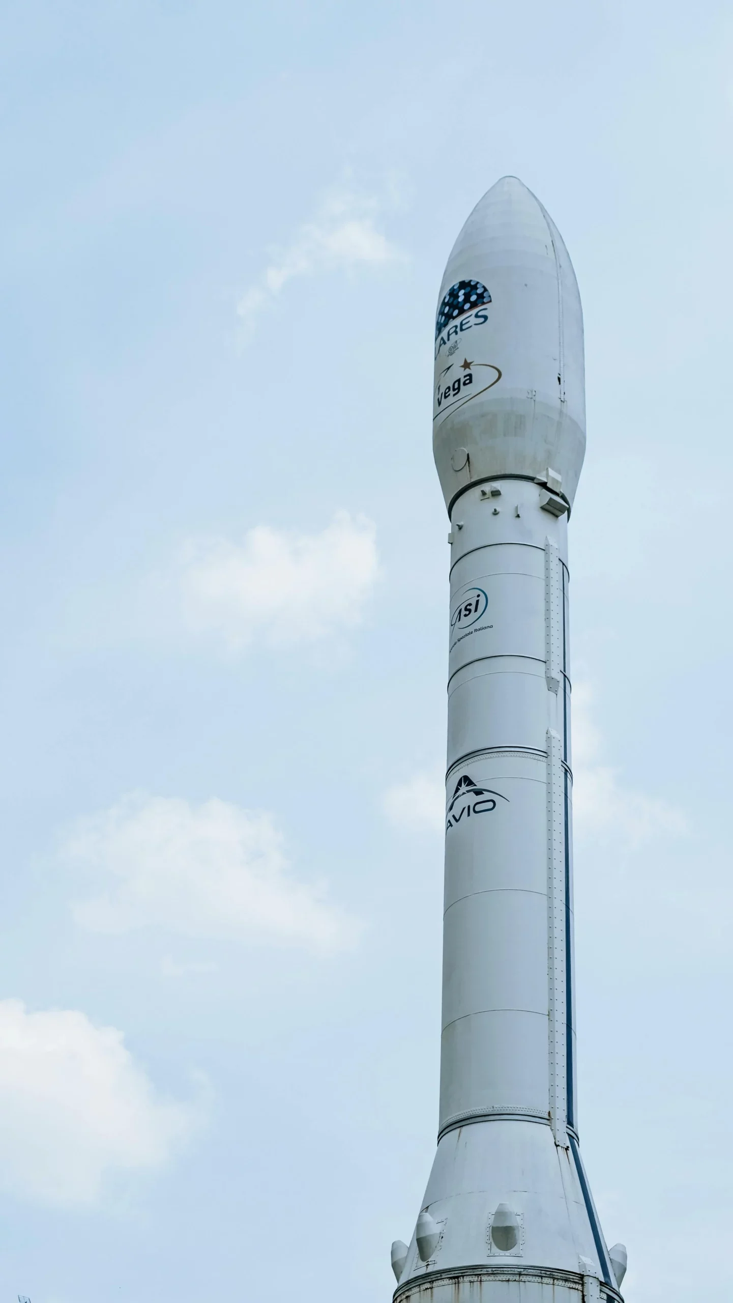 White Vega rocket standing upright against a pale blue sky with light clouds