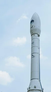 White Vega rocket standing upright against a pale blue sky with light clouds