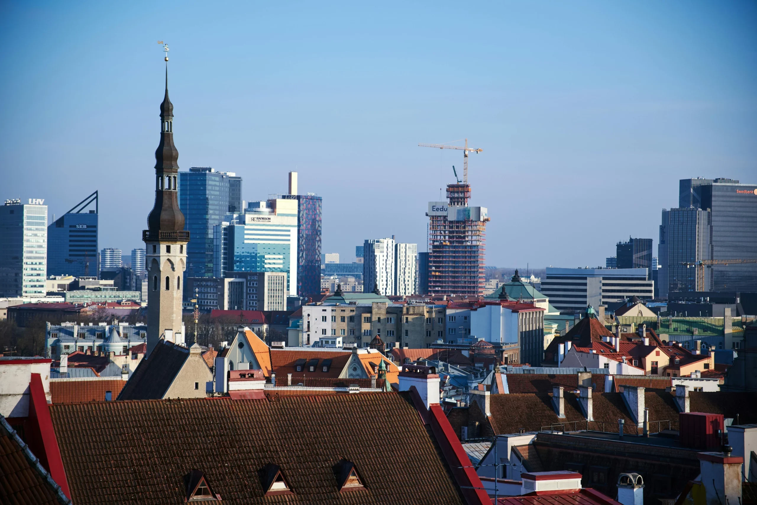 City skyline with a church spire, red tile rooftops and glass towers under a clear blue sky