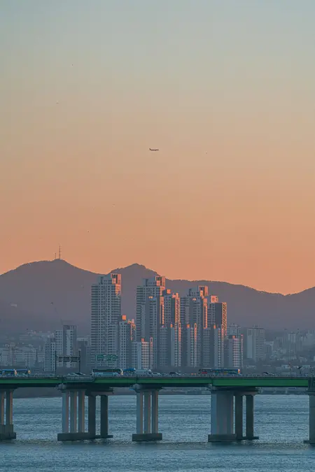 Sunset over a river bridge and high-rise apartment towers in front of hills