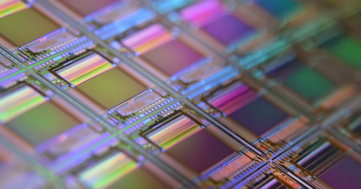 Macro view of a silicon wafer with rows of colourful chip dies catching rainbow light