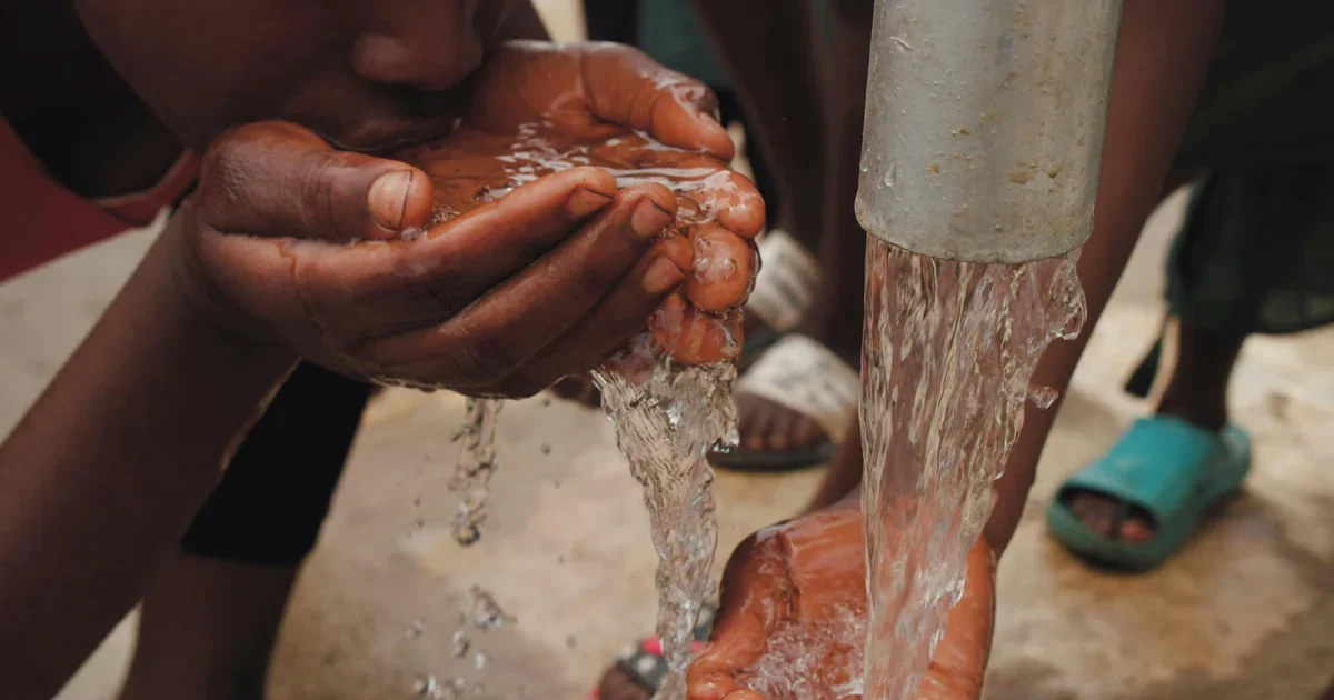 Hands cupped under water flowing from a metal tap pipe as people drink and wash