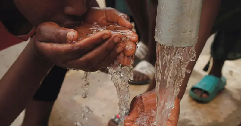 Hands cupped under water flowing from a metal tap pipe as people drink and wash