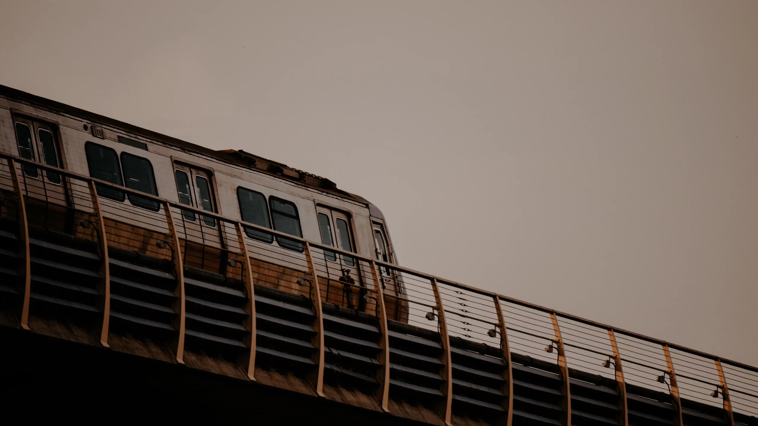 Elevated metro train running along a railed viaduct against a hazy brown sky