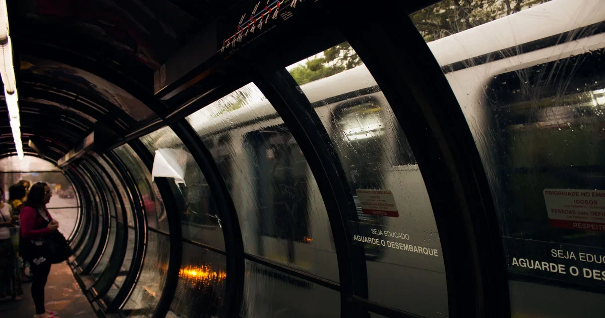 Tube-shaped glass bus station with a bus passing and a passenger waiting at the left